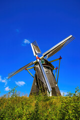 Fototapeta premium Beesel, Netherlands - July 9. 2021: View on isolated typical dutch windmill (Molen de grauwe beer) in rural landscape against deep blue summer sky with cumulus clouds