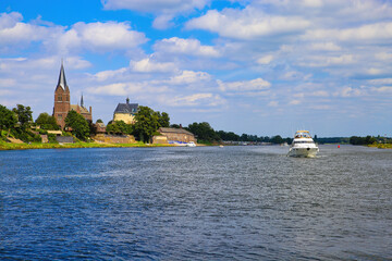 View over river maas on old villaga with church tower, motor boat against blue summer sky - Kessel,...