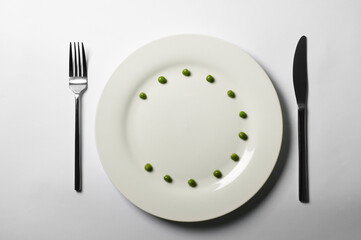 Place setting with plate, 12 green peas, fork, and knife. Top view.