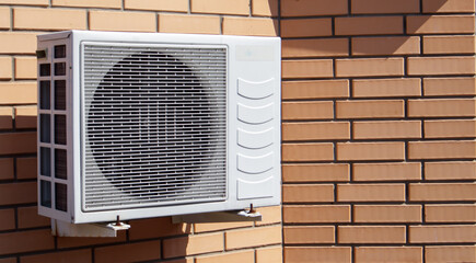 Close-up shot of a modern climate control unit against the background of a brick wall of the facade of a house outside. Air conditioner on the wall with space for text. Air compressor.