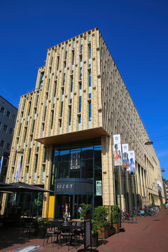 Arnhem (Rozet Centrum), Netherlands - July 9. 2021: View on entrance of modern architecture building in city center with outdoor restaurant cafe against blue summer sky