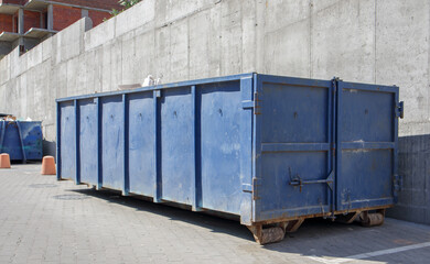 Metal durable blue industrial trash bin for outdoor trash at construction site. Large waste basket for household or industrial waste. A pile of waste.