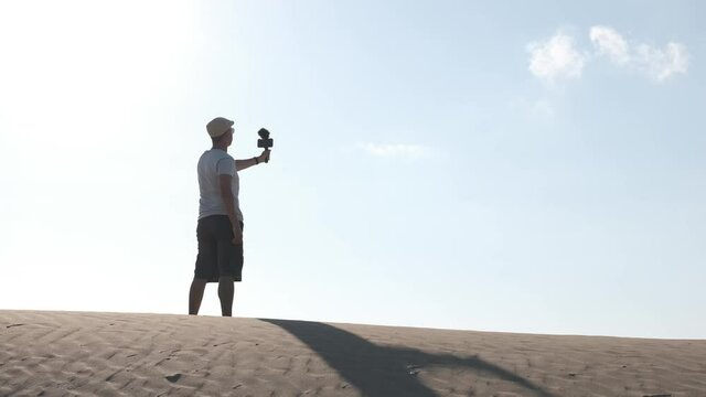 Man filming himself with his cell phone in the desert dunes. Traveling male content creator
