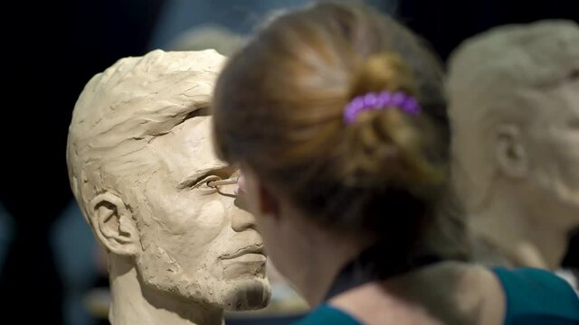 Woman sculptor at work on a sculpture of a human head. The process of restoring the shape of the eyes. Side view. Close up view.