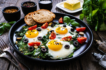 Sunny side up eggs with spinach, cherry tomatoes and black olives on wooden table
