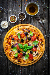 Circle pizza with mozzarella, white mushrooms, salami and tomatoes on wooden table
