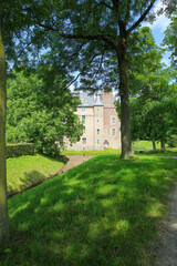 Fototapeta na wymiar View beyond green trees on dutch water castle from 14th century against blue summer sky