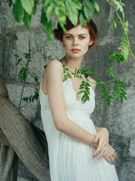 attractive woman in white dress near tree basing stone wall