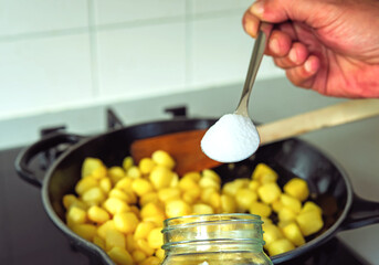 A hand holding full spoon of salt. A man cooking fried potato with too much salt for seasonings ....