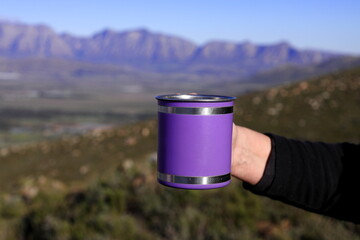 A hand shown holding a purple, metallic mug