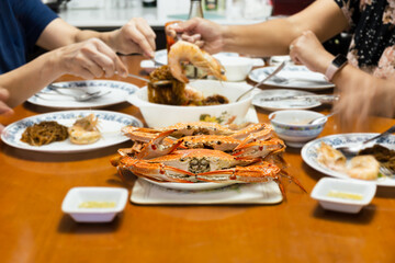 Asian family having dinner with fresh steamed blue crabs seafood at home. indoor