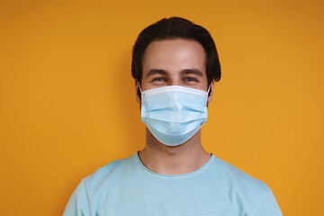 Portrait of young man in protective face mask looking at camera while standing against yellow background