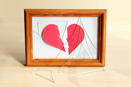 Two halves of a torn paper heart under shards of glass in a photo frame