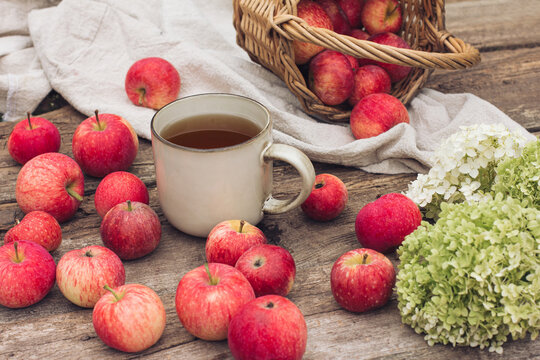 A cup of tea, fresh red apples and hydrangea flowers on a textured wooden background. Autumn day and image, autumn photography, food decor, light