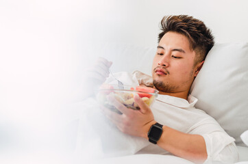 Portrait of young handsome Chinese man eating a fresh, delicious and healthy tomate salad with tune on the sofa in the living room of a minimalist and clean home