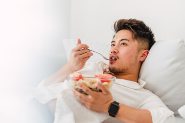 Portrait of young handsome Chinese man eating a fresh, delicious and healthy tomate salad with tune on the sofa in the living room of a minimalist and clean home