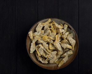 Marinated parts artichoke in oil with herbs, top view. Artichoke in a bowl on a black wood background.
