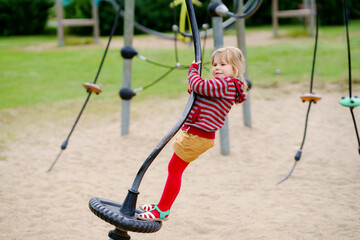 Little preschool girl playing on outdoor playground. Happy toddler child climbing and having fun with summer outdoors activity.