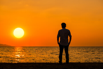 Silhouette businessman show relax after work standing on the beach at sunset time with sunlight sky background.