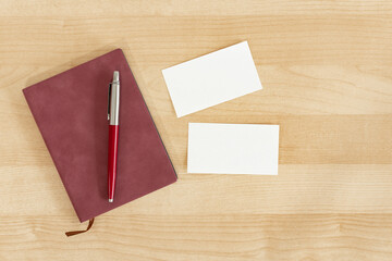Blank business cards, burgundy notebook and pencil on wooden office table. Business card Mock Up.