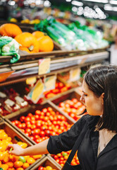 Woman chooses and purchases fresh ripe organic tomatoes in vegetable department of supermarket
