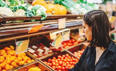 Woman chooses and purchases fresh ripe organic tomatoes in vegetable department of supermarket
