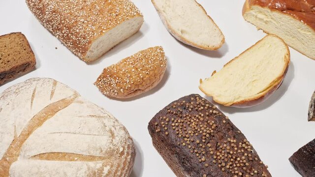 Top view collection of different fresh bakery breads with seeds, coriander, brioche, rye, with cut loaf slices