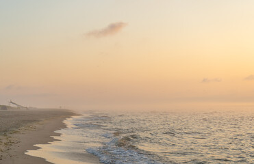 Foggy sunrise over the sea. Pastel shades. Beautiful landscape. Sandy beach of the ocean. Sunset sky. Clouds. Coast.