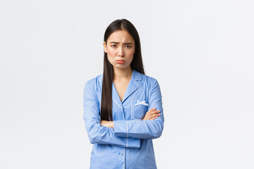 Offended silly insecure asian girl in blue pajamas, cross hands chest and sobbing, pouting and...