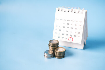 stack of coins and calendar on blue background