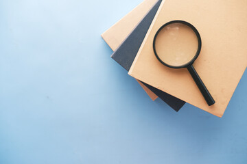 stack of book and magnifying glass on blue background .