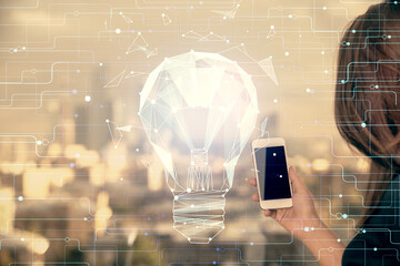 Double exposure of light bulb hologram and woman holding and using a mobile device. Idea concept.