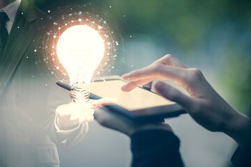 Double exposure of light bulb hologram and woman holding and using a mobile device. Idea concept.