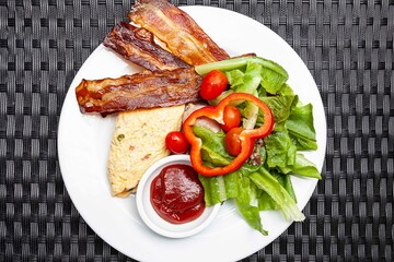 Western breakfast, scrambled eggs, bacon and fresh vegetables with tomato sauce