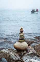 Fototapeta na wymiar Stack of stones near the sea with a boat at background.