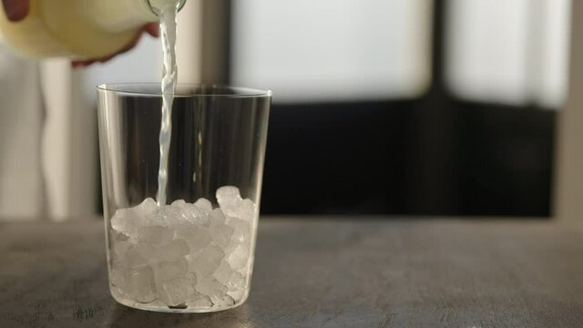 Slow motion pour lemonade into tumbler glass with crushed ice on oak table