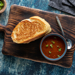 Top down view of a grilled cheese sandwich served with tomato soup on a wooden board. 