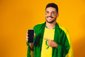 Brazilian fan. portrait, brazilian fan showing his cell phone, dressed as a football fan or soccer match on yellow background. Colors of Brazil. world Cup.