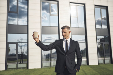 Confident mature businessman holding coffee cup while standing near office building