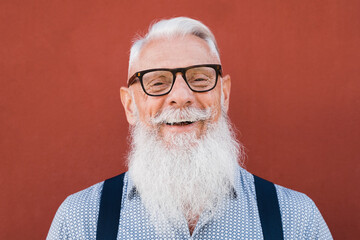 Portrait of happy hipster senior man smiling on camera with red background - Focus on face
