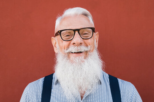 Portrait Of Happy Hipster Senior Man Smiling On Camera With Red Background - Focus On Face