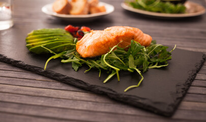 Baked sea trout fillet with fresh vegetables and herbs on black board