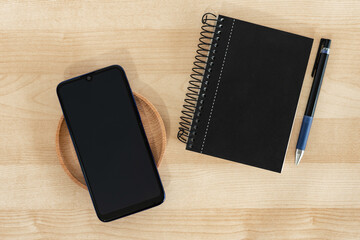 Smart phone, notebook and pen in black color, on wood background. Office style.