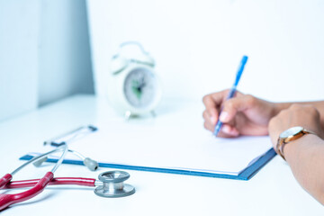The doctor is writing the patient's condition diary. on the white table There is a stethoscope and recording paper in the office at the hospital.