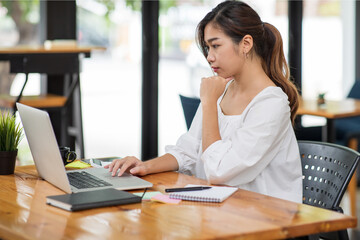 Confident Asian young businesswoman working on laptop at her workplace at modern office.Blurred background.