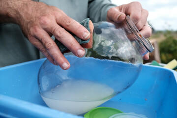 Male hands wash a dirty glass jar with a sponge, in a plastic basin, in a village courtyard, outdoors. Rural traditions. 