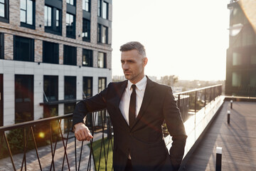 Confident mature man in full suit standing on business center terrace