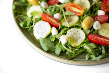 Arugula, tomato, cucumber, mozzarella and olive salad in a green plate.