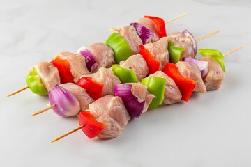 Raw chicken and vegetable skewers with bell peppers and onion on white marble background. close up