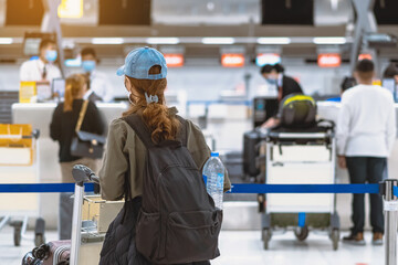 Back view of airline passenger wear face mask to prevent Corona virus (Covid-19) wait to check in counter in airport with staff wear face mask. New normal concept of travel after Covid-19 pandemic.
